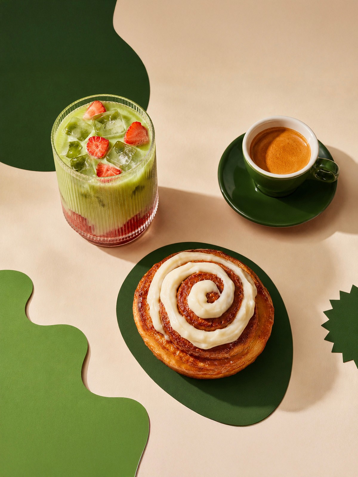 Overhead view of an iced strawberry matcha, a cup of espresso, and a frosted cinnamon roll.